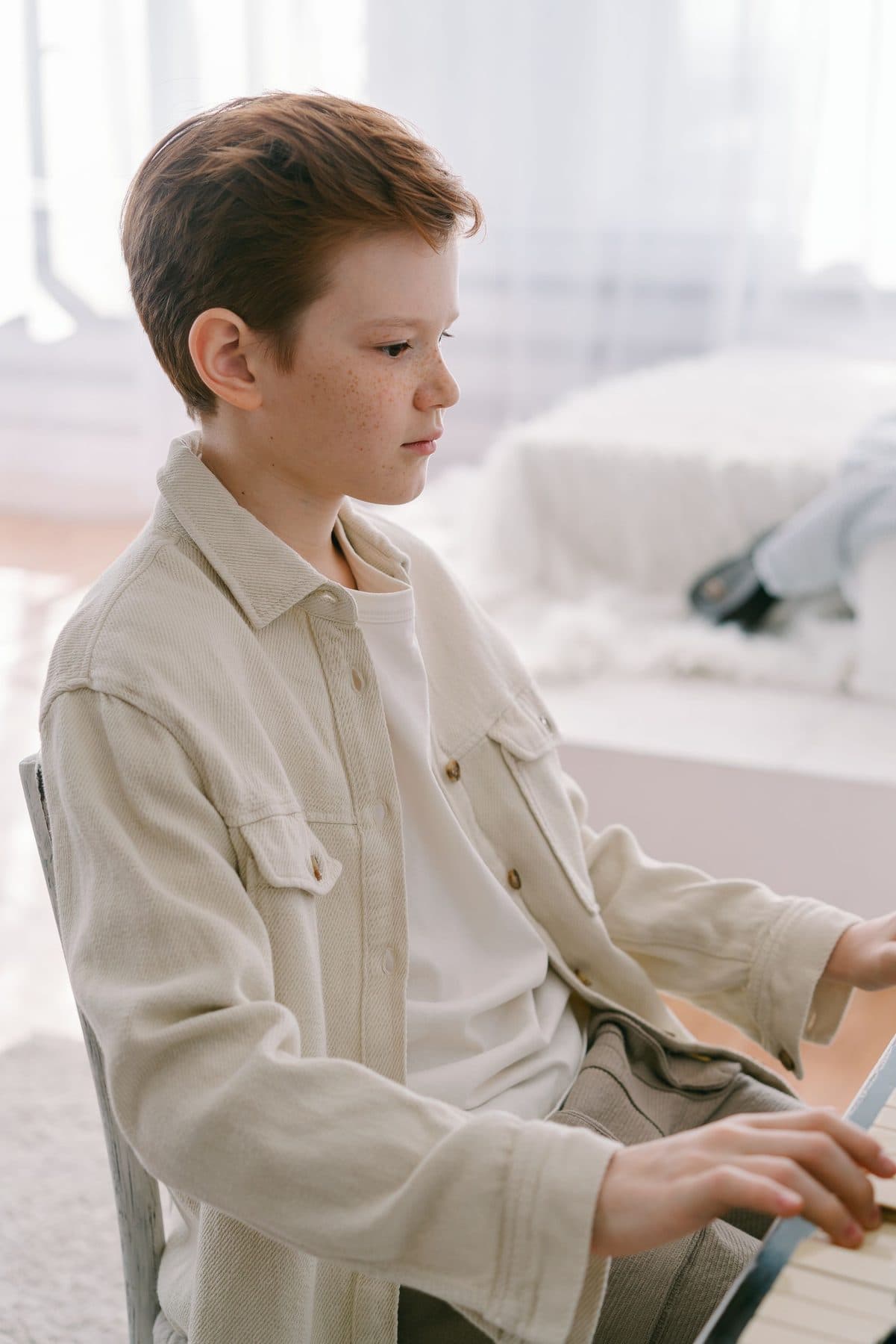 A young boy in a blue shirt seated at a piano, seen from the side.