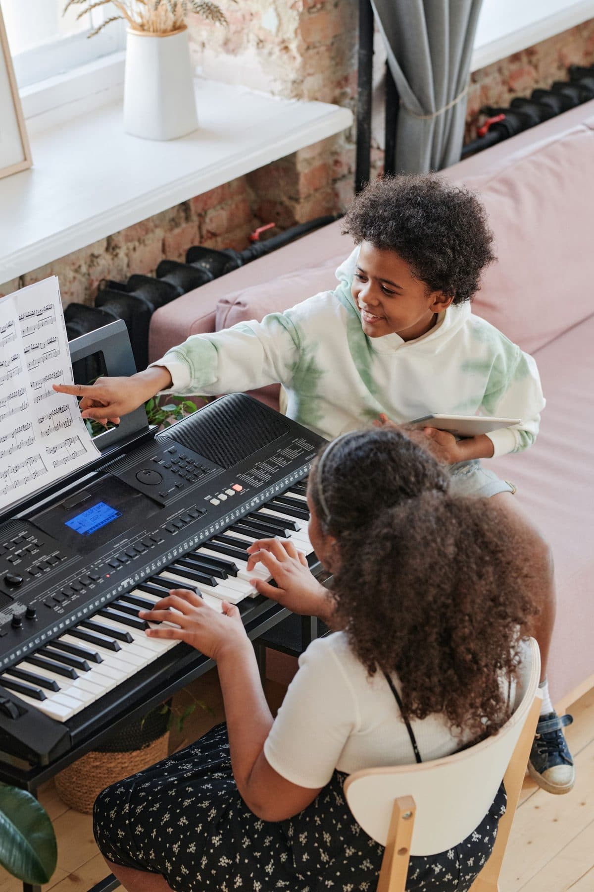 Two children sitting together at a piano, looking toward the keys.