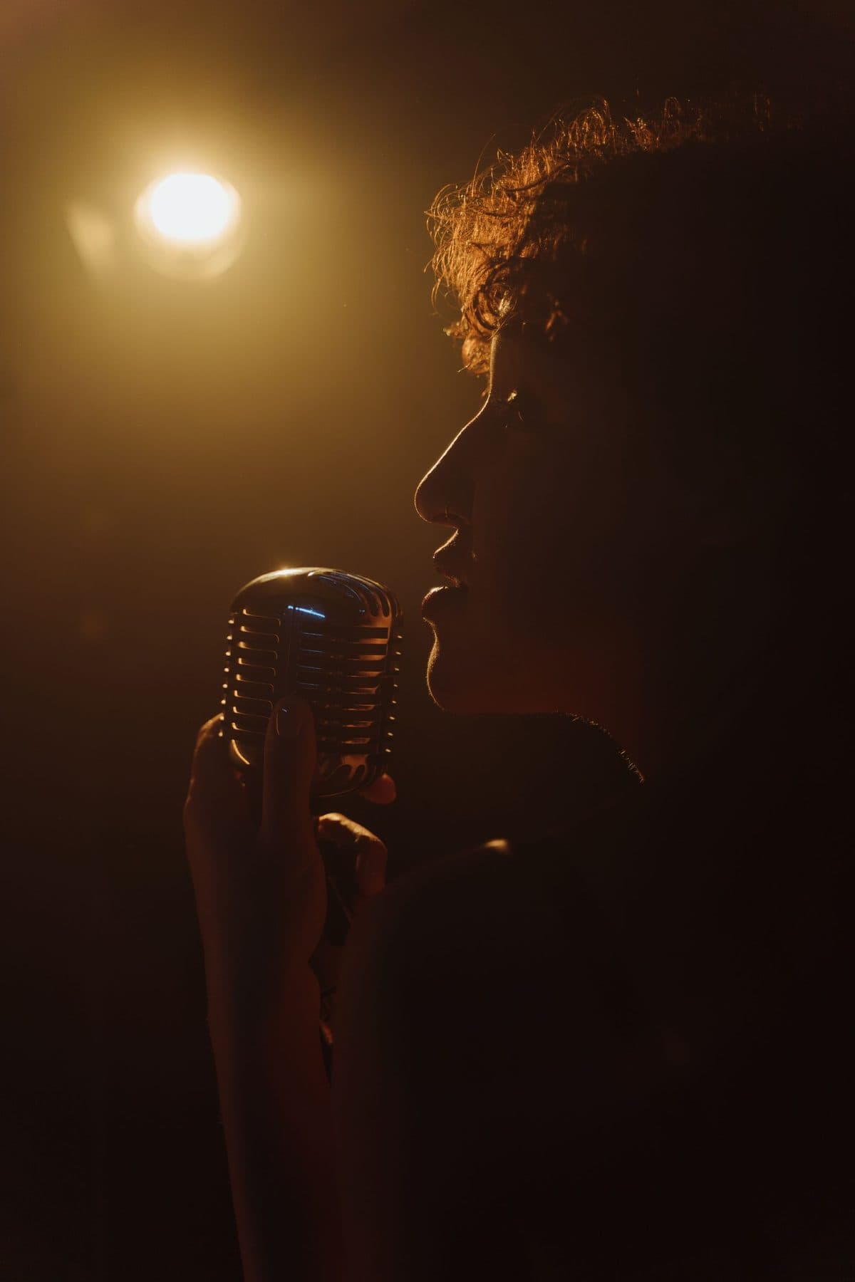 A person singing into a microphone under warm light.